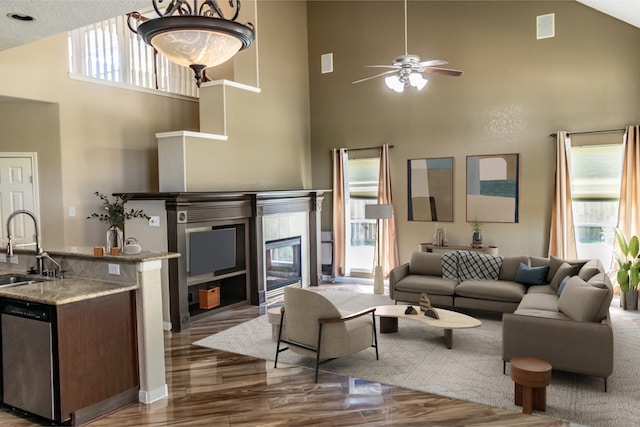 living area with a high ceiling, ceiling fan, a tiled fireplace, and wood finished floors