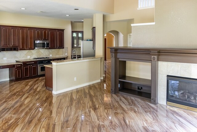 kitchen with a wealth of natural light, dark hardwood / wood-style flooring, a tiled fireplace, and appliances with stainless steel finishes