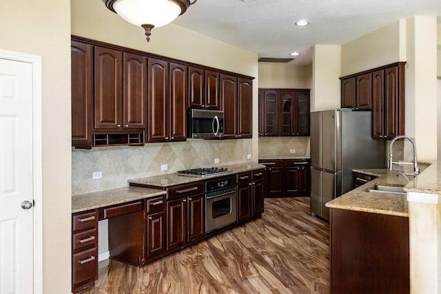 kitchen with dark brown cabinetry, stainless steel appliances, a sink, backsplash, and light stone countertops