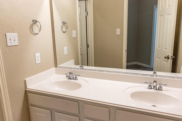 bathroom featuring a textured wall, double vanity, and a sink