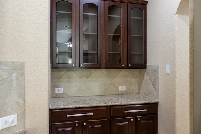 bar featuring light stone counters, decorative backsplash, and dark brown cabinets