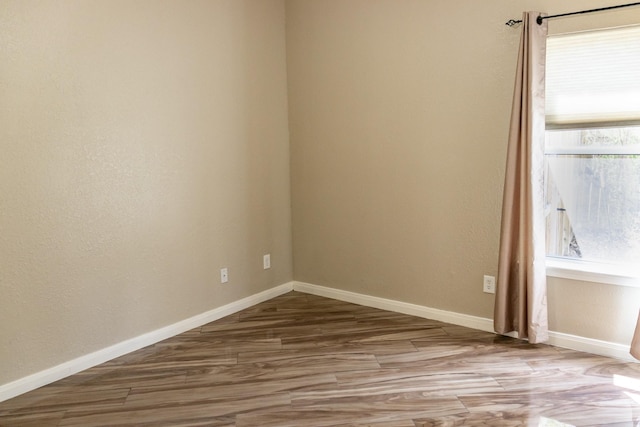 spare room with baseboards and wood finished floors