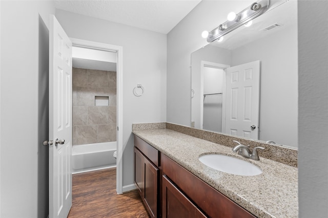 full bathroom featuring hardwood / wood-style floors, tiled shower / bath combo, vanity, and toilet