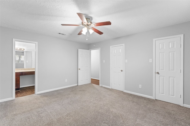 unfurnished bedroom with ceiling fan, connected bathroom, a textured ceiling, built in desk, and carpet