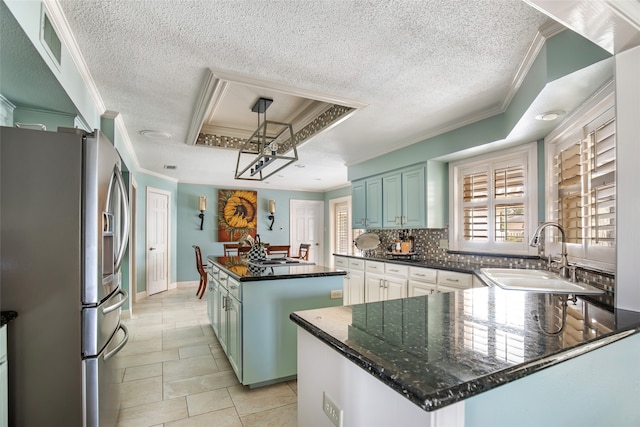 kitchen with sink, a raised ceiling, a center island, stainless steel fridge, and crown molding