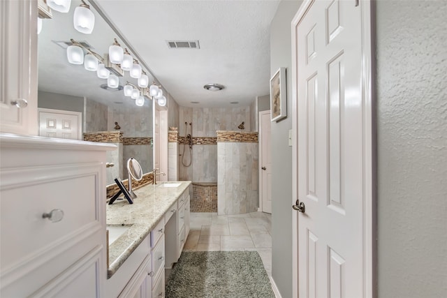 bathroom with vanity, a tile shower, a textured ceiling, and tile patterned floors