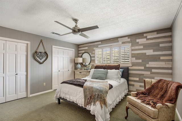 carpeted bedroom with ceiling fan, wood walls, a textured ceiling, and two closets