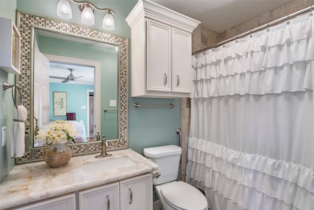 bathroom with ceiling fan, a textured ceiling, toilet, vanity, and curtained shower