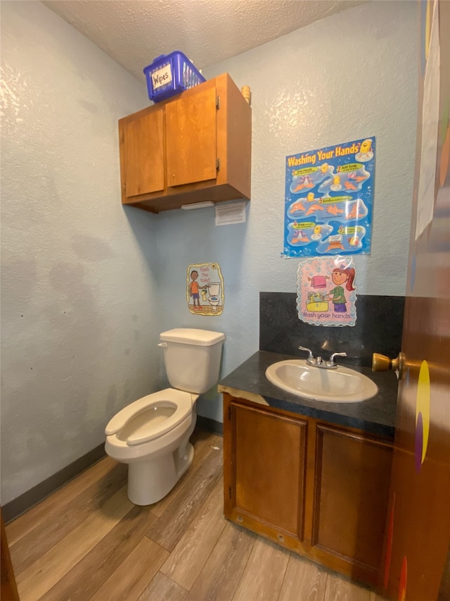 bathroom featuring wood-type flooring, a textured ceiling, vanity, and toilet