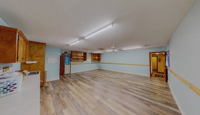 basement featuring a textured ceiling, ceiling fan, and light wood-type flooring