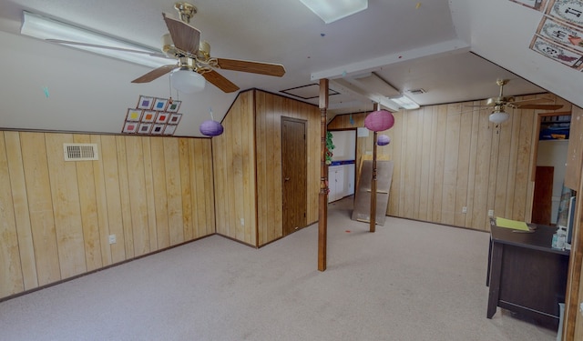 basement featuring wood walls, light colored carpet, and ceiling fan