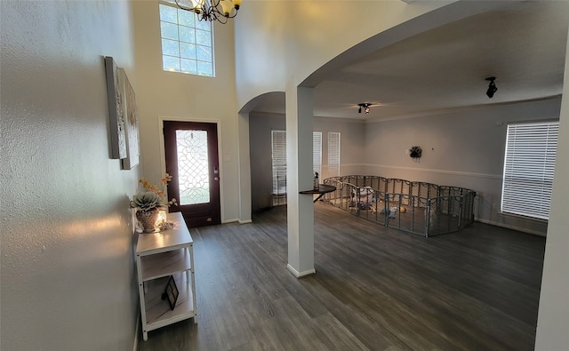 foyer with a towering ceiling, dark hardwood / wood-style floors, an inviting chandelier, and ornamental molding