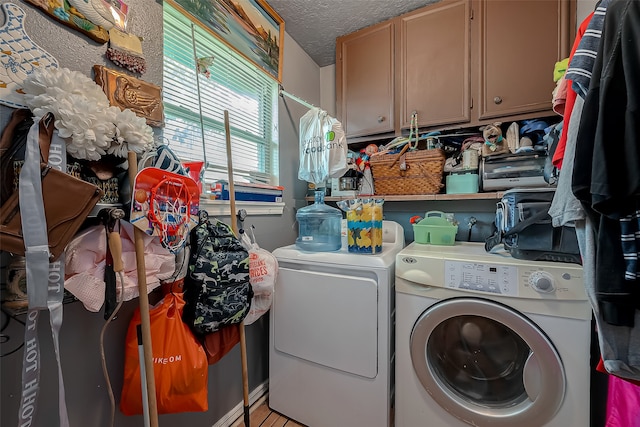 clothes washing area featuring a textured ceiling, washer and clothes dryer, and cabinets