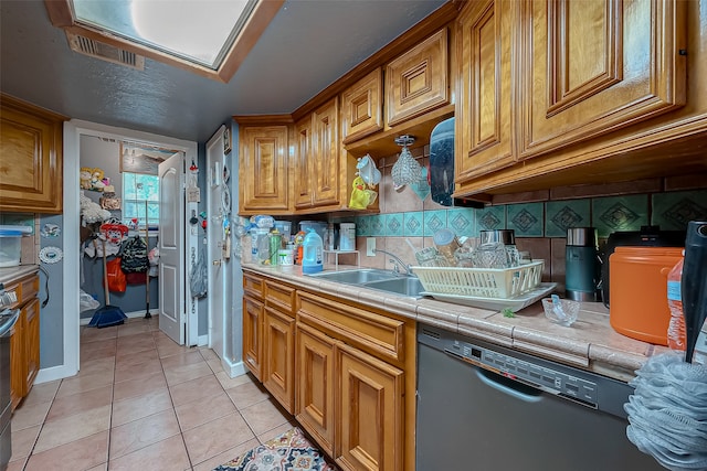 kitchen featuring backsplash, sink, light tile patterned floors, tile counters, and black dishwasher