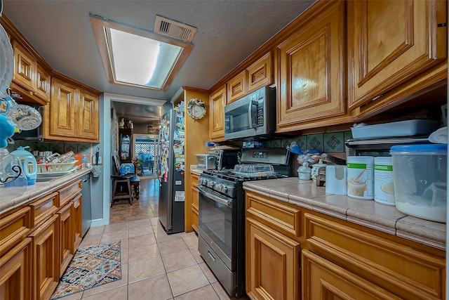 kitchen featuring light tile patterned floors, decorative backsplash, stainless steel appliances, and tile countertops