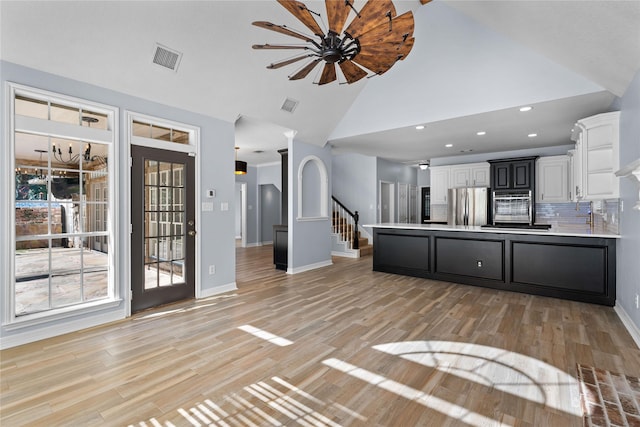 kitchen featuring high vaulted ceiling, white cabinets, decorative backsplash, light wood-type flooring, and stainless steel appliances