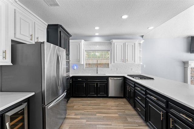 kitchen featuring appliances with stainless steel finishes, backsplash, sink, white cabinets, and wine cooler