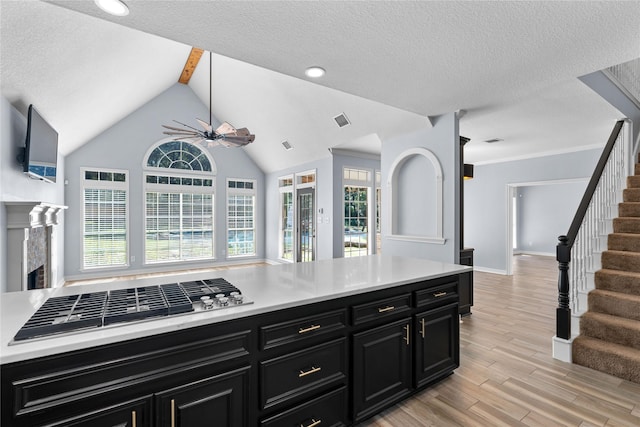 kitchen featuring a textured ceiling, ceiling fan, a fireplace, vaulted ceiling with beams, and stainless steel gas stovetop