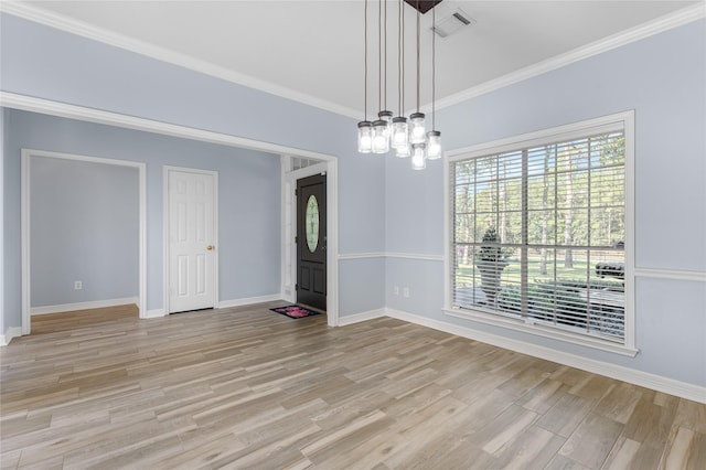 empty room featuring a notable chandelier, light wood-type flooring, and crown molding