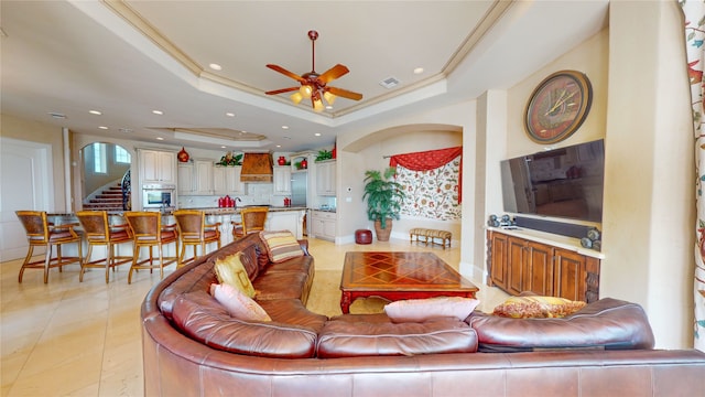 tiled living room featuring a tray ceiling, ceiling fan, and ornamental molding