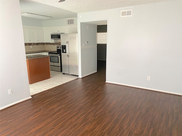 kitchen with a textured ceiling, stainless steel appliances, decorative backsplash, light wood-type flooring, and white cabinets