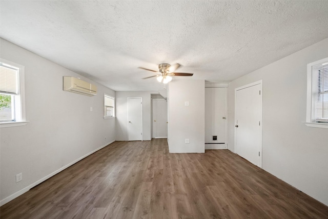 unfurnished room featuring a wall unit AC, wood finished floors, a ceiling fan, and a textured ceiling