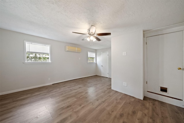 unfurnished bedroom featuring multiple windows, a wall mounted AC, and wood finished floors