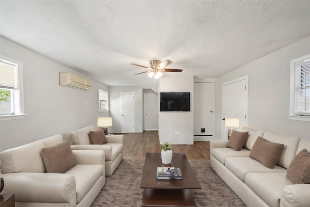 living area with a textured ceiling, an AC wall unit, ceiling fan, and wood finished floors