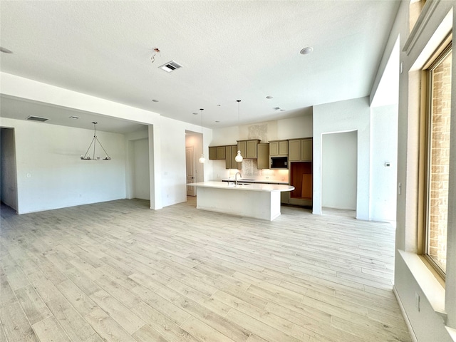 kitchen featuring tasteful backsplash, a kitchen island with sink, hanging light fixtures, and light hardwood / wood-style floors