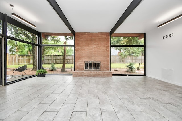 unfurnished living room with beamed ceiling, a brick fireplace, brick wall, and light tile patterned floors