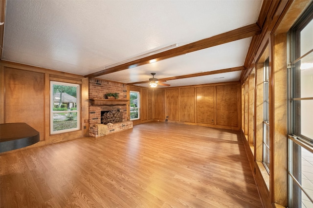 unfurnished living room with beam ceiling, a fireplace, light hardwood / wood-style floors, and wooden walls