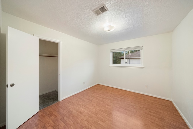 unfurnished bedroom with a closet, wood-type flooring, a spacious closet, and a textured ceiling