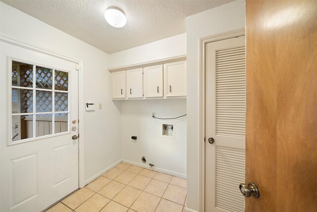 clothes washing area with a textured ceiling, hookup for a washing machine, cabinets, light tile patterned floors, and electric dryer hookup