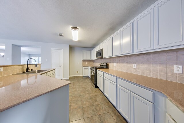 kitchen with stainless steel appliances, decorative backsplash, white cabinetry, sink, and light tile patterned floors