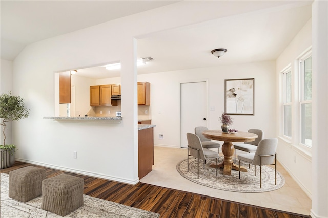 kitchen featuring light stone counters, kitchen peninsula, hardwood / wood-style floors, and exhaust hood