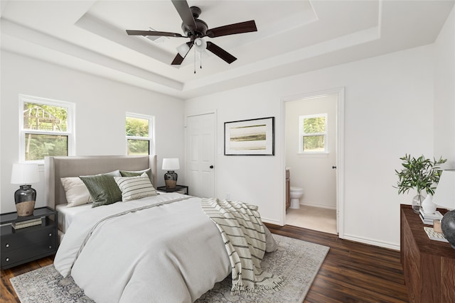 bedroom with a raised ceiling, dark wood-type flooring, and multiple windows