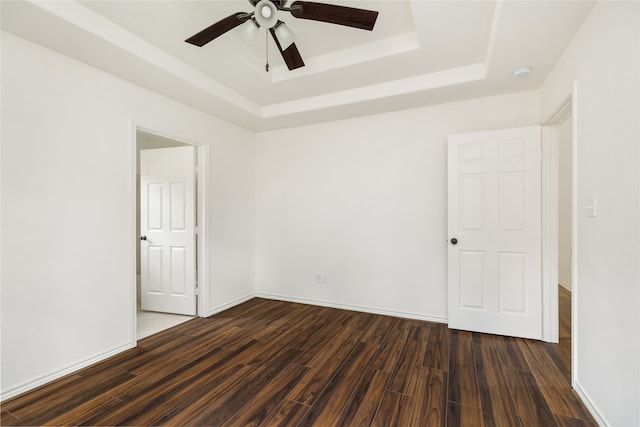 empty room featuring ceiling fan, dark hardwood / wood-style floors, and a tray ceiling