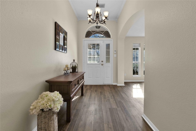 foyer entrance with crown molding, dark wood-type flooring, and a chandelier