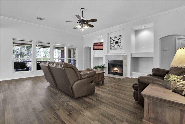 living room with ceiling fan, crown molding, dark wood-type flooring, and a fireplace