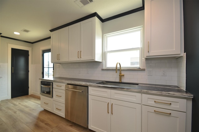 kitchen with stainless steel appliances, a sink, visible vents, light wood finished floors, and crown molding