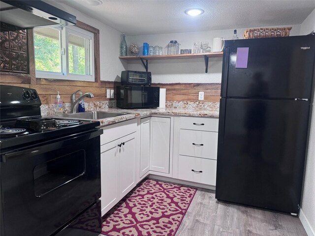 kitchen featuring white cabinets, light hardwood / wood-style floors, sink, wall chimney range hood, and black appliances