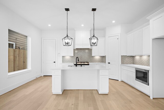 kitchen featuring white cabinetry, light hardwood / wood-style floors, tasteful backsplash, and stainless steel microwave