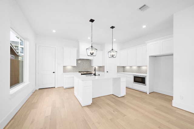 kitchen featuring light countertops, visible vents, stainless steel microwave, decorative backsplash, and light wood-type flooring