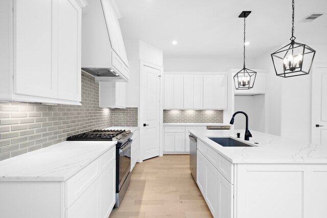 kitchen featuring decorative light fixtures, stainless steel appliances, sink, a center island with sink, and light hardwood / wood-style floors