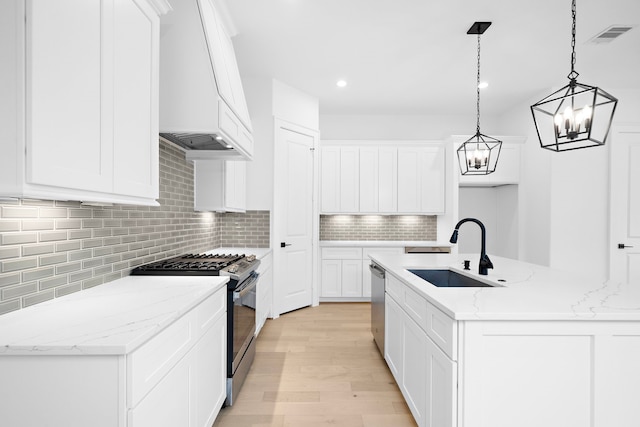 kitchen with custom exhaust hood, tasteful backsplash, light wood-style flooring, appliances with stainless steel finishes, and a sink