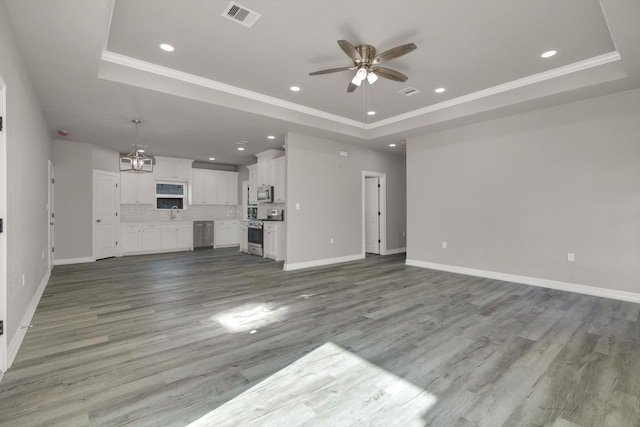 unfurnished living room featuring light wood-type flooring, a tray ceiling, ceiling fan, and ornamental molding