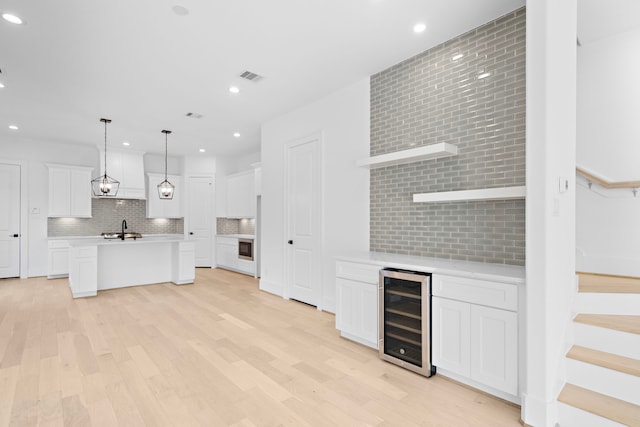 unfurnished living room featuring wine cooler, sink, and light wood-type flooring