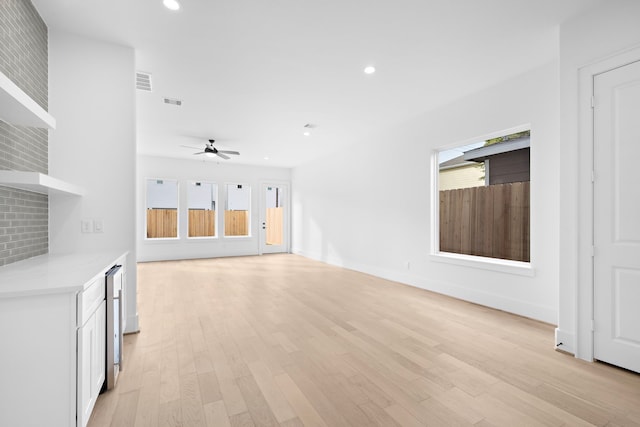 unfurnished living room with beverage cooler, ceiling fan, and light hardwood / wood-style floors