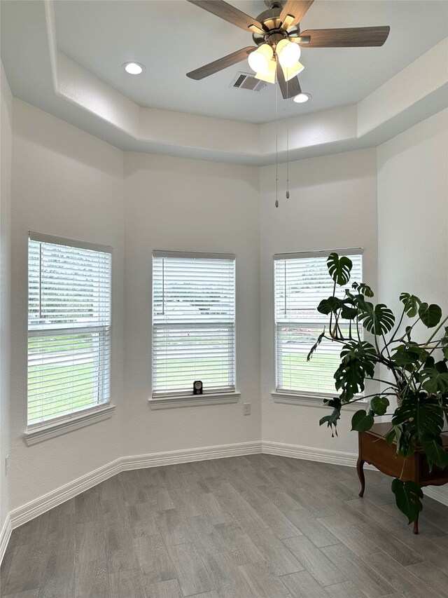 unfurnished room featuring a wealth of natural light, a tray ceiling, visible vents, and wood finished floors