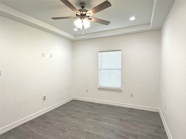 spare room featuring a tray ceiling, dark wood finished floors, a ceiling fan, and baseboards